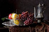 Obststillleben im Stil eines Gemäldes mit Apfel, Zitrone, Trauben und Silberkanne