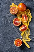 Sliced and whole ripe juicy Sicilian Blood oranges fruits with knife and yellow textile on black concrete texture