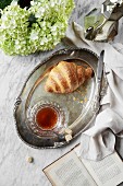 Frühstück mit Croissant und Tee auf Silbertablett (Aufsicht)
