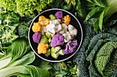 Variety of raw green vegetables salads, lettuce, bok choy, corn, broccoli, savoy cabbage round colorful young cauliflower in black bowl