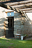 Old wooden chair next to exterior door of stone house below pergola