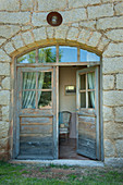 Open double doors with fan light and arched frame leading into old stone house