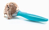 A scoop of chocolate ice cream in a blue ice cream scoop against a white background