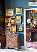 Antique gilt-framed pictures on blue wall above old wooden chest of drawers