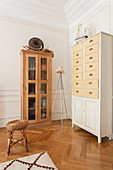Wooden display case and chest of drawers on parquet floor against panelled walls