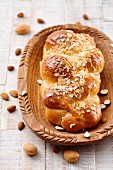 A yeast bread plait with almond flakes in a wooden bowl