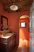 Washstand with wooden base unit in bathroom with terracotta walls and arched open doorway