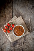 Tomato chutney in a small bowl on a sackcloth on a wooden background