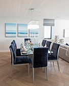 Blau gepolsterte Stühle um Esstisch vor Bilder mit Meer-Motiv in offenem Wohnraum