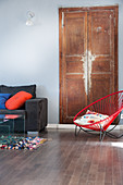 Red designer easy chair in front of worn wooden door in living room