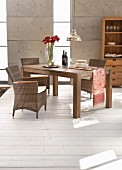 Elegant rattan armchairs and solid-wood table in front of concrete wall with vertical glazed stripes