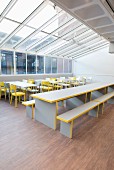 Tische, Stühle und Bänke in Grau und Gelb unter einem Glasdach