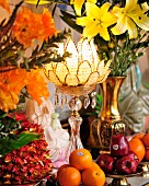 Flower-shaped candle lantern amongst opulent arrangement of flowers and fruit