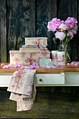 Romantic vintage-style still-life arrangement of peonies and decorative cardboard boxes against rustic board wall