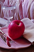 Pink apple and cutlery on pink plate next to glass of water