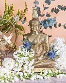 Buddhafigur mit weißen Blüten und Distelblüten dekoriert