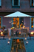 Fire bowls and candle lanterns arranged around pool in front of terrace in summer twilight
