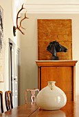 Ceramic pot on exotic-wood table in front of bust of horse and hunting trophy