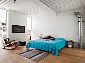 Doppelbett mit blauer Tagesdecke und Schaukelstuhl im Schlafzimmer mit weiss gestrichenen Betonblöcken