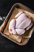 Raw organic uncooked whole chicken with salt and pepper on backing paper in old oven tray