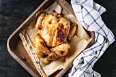 Grilled baked whole organic chicken on backing paper in old oven tray with white kitchen towel and meat fork