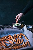 Woman dipping oven baked sweet potatoe fries into avocado sauce