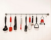 Black and red kitchen utensils hung from hooks on bar
