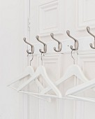 White coathangers hung from row of hooks on panelled door