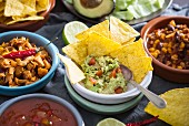 Vegan Mexican dishes: guacamole with tortilla chips, salsa, chopped jackfruit, and chilli con carne