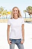 Blonde Frau in weißem T-Shirt und Jeanshose am Strand