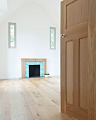 View into empty, high-ceilinged room with open fireplace between windows in gable-end wall