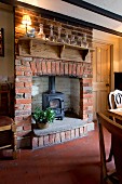 Log-burning stove in traditional brick fireplace below glass carafes on rustic bracket shelf