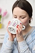 Young woman drinking from white DIY Easter mug with hand-drawn bunny motif