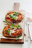 Two homemade glutenfree mini pizzas with cauliflower, pumpkin and rocket on wooden board