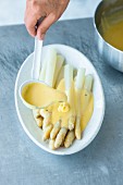 Hollandaise sauce being poured over white asparagus