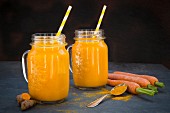 Carrot and turmeric smoothie in two glasses with straws