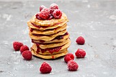 A stack of pancakes with raspberry sauce and raspberries