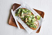 A green open sandwich with grilled chicken breast, avocado, cucumber and mushy peas