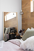 Bed, bedside table and mirror in bedroom with wall made from recycled oak