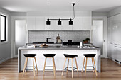 Fitted kitchen with subway tiles, kitchen counter with bar stools and black light in an open living room