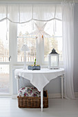 Halbrunder Tisch mit winterlicher Deko vor dem Fenster mit weißer Gardine