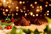 Ilex auf Holztisch mit einem Haufen Kakaopulver, Kakaobohnen und Schokoröllchen (weihnachtlich)