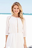 A blonde woman wearing a white summer dress with lace panel on the beach