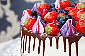 A cake with meringue kisses, fresh strawberries, blueberries, raspberries and chocolate sauce