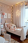 Cosy lighting around bed in girl's bedroom in pastel shades
