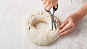 Cutting an wreath of bread dough with scissors