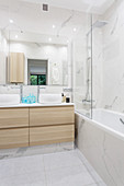Bathtub with glass screen and twin washstand in elegant bathtub with marble tiles