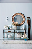 Round wall mirror over a half-high shelf with maritime decorative objects