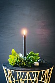 Lit black candle in hand-made wreath of leaves