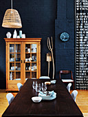 Dining table with chairs and display cabinet made of wood in an open living room with a dark blue wall